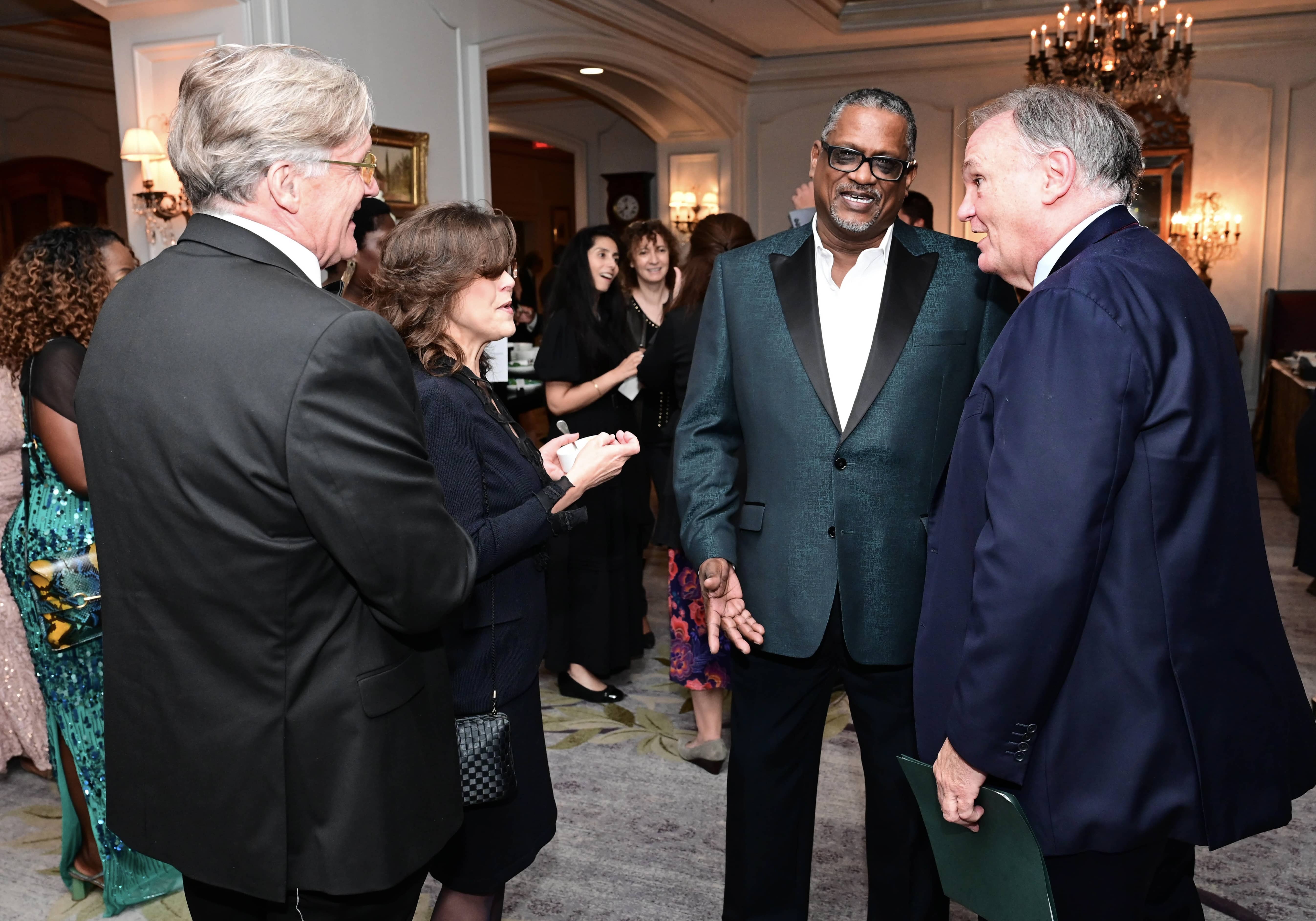 Four people, including a man in a green tuxedo jacket, smile and converse at a formal event.