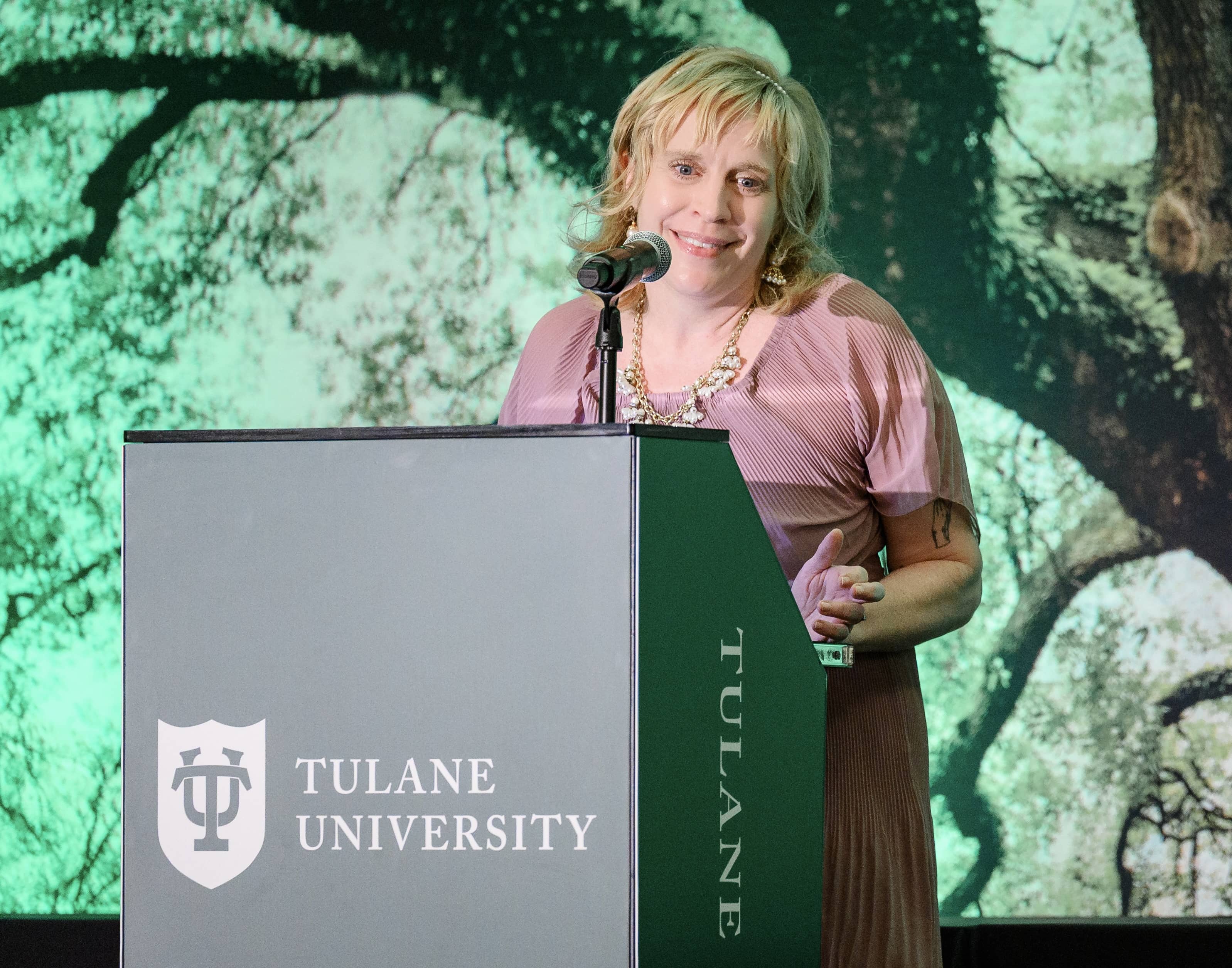 Blonde woman in a pink dress smiles behind a Tulane University podium.