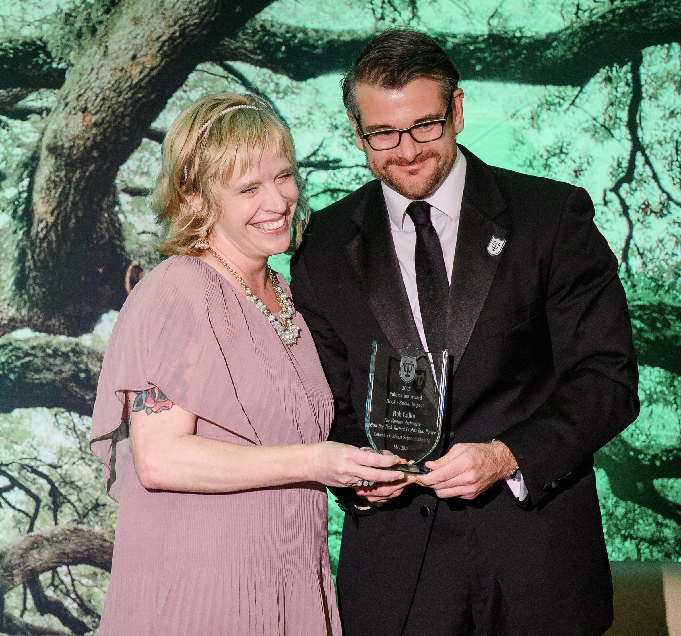 Woman presenting a glass award to a man in a tuxedo.