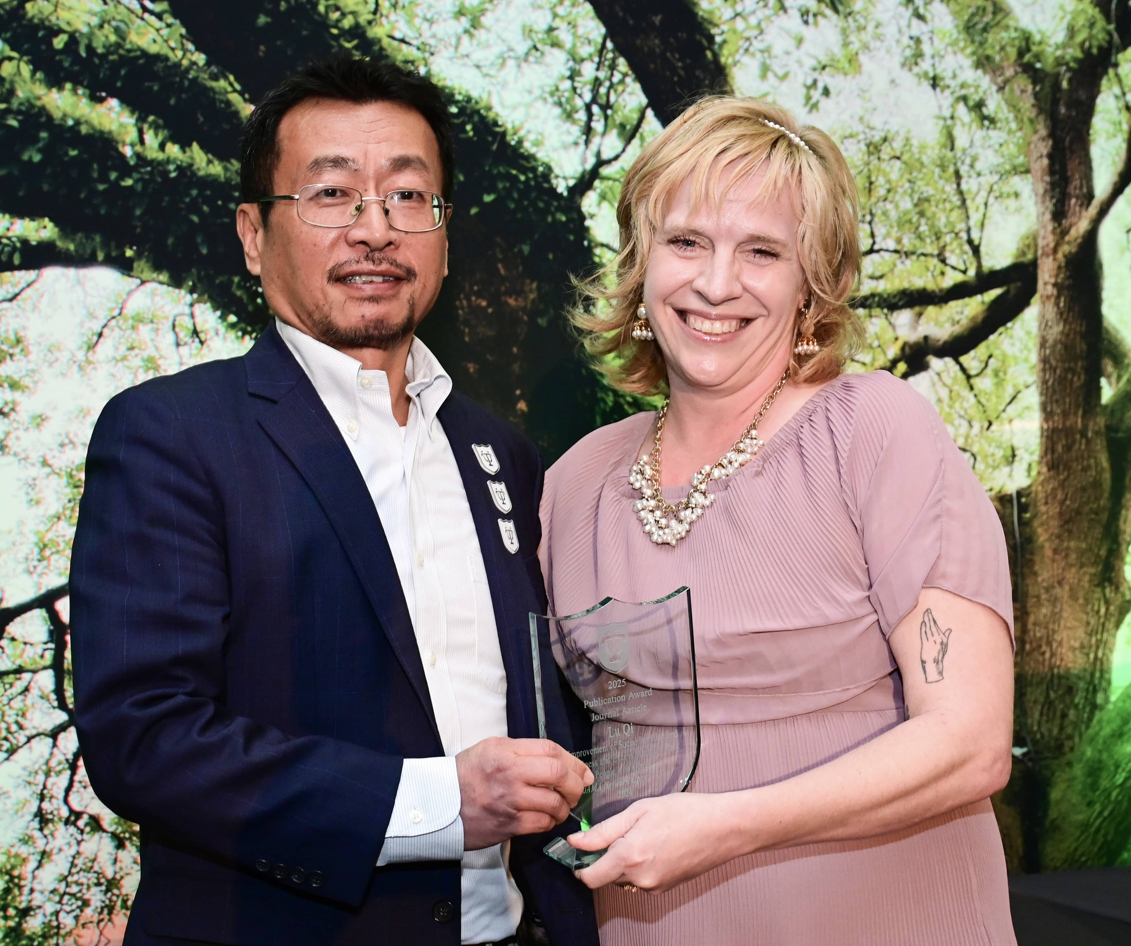 Smiling man in suit receives a glass award to a smiling woman.
