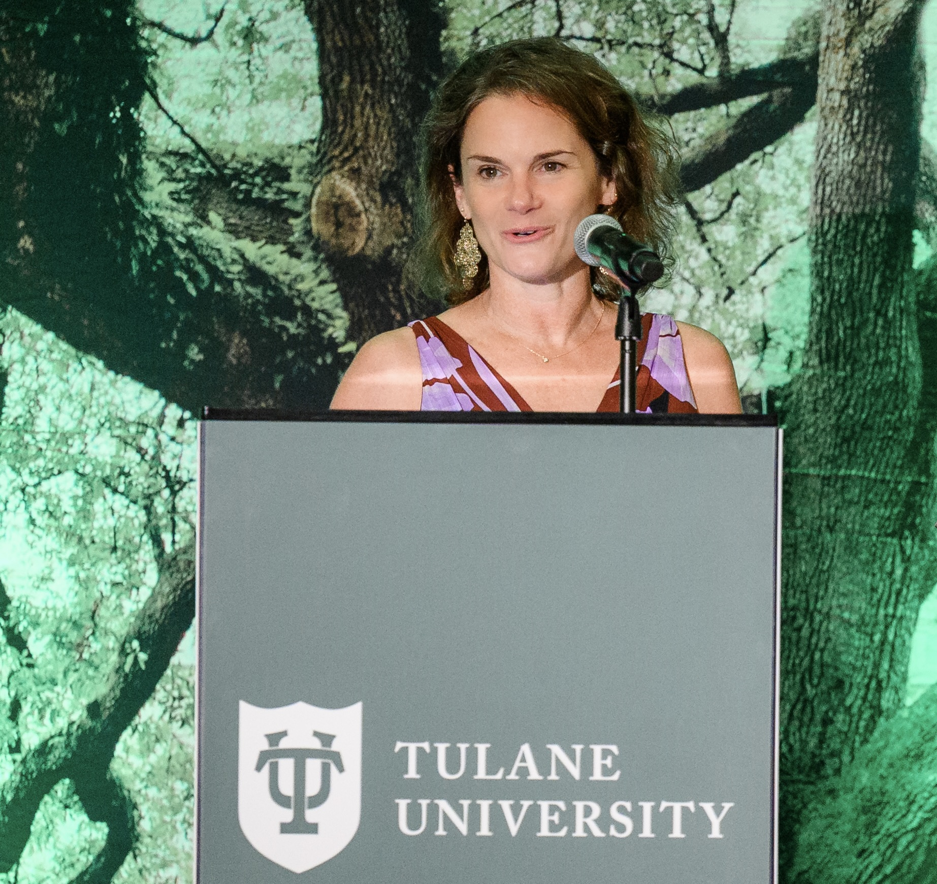 Woman speaking into microphone at a podium with Tulane University logo.