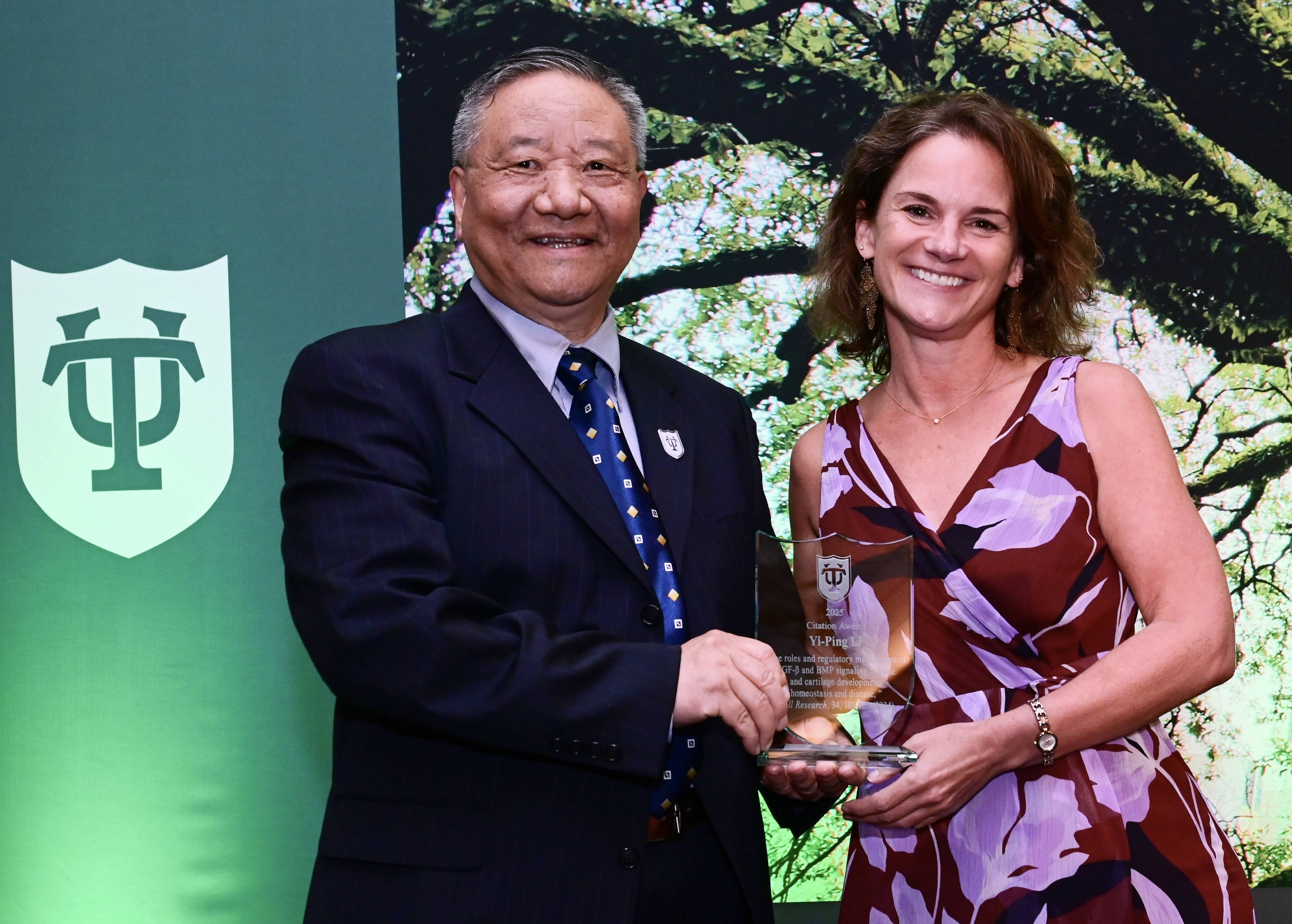 Smiling woman presents award to a man in suit against green background.
