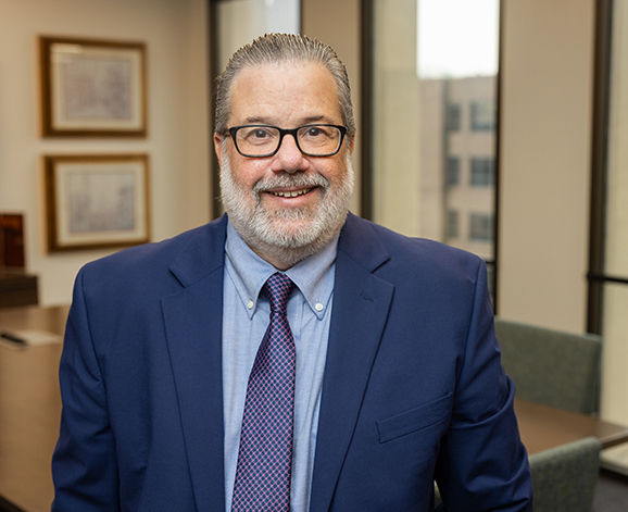 Professional portrait of a smiling man in a blue suit and tie.